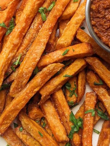 A plate of sweet potato fries with a tomato dipping sauce at the side.