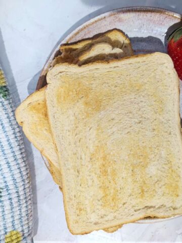 Two slices of toast on a plate with fresh strawberries beside them.