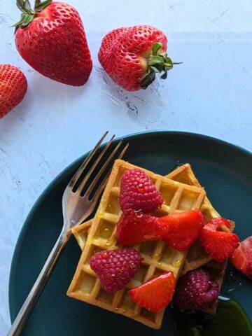 Two waffles on a plate topped with strawberries and raspberries.