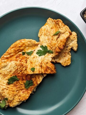 Two turkey breast steaks topped with herbs and spices on a blue plate.